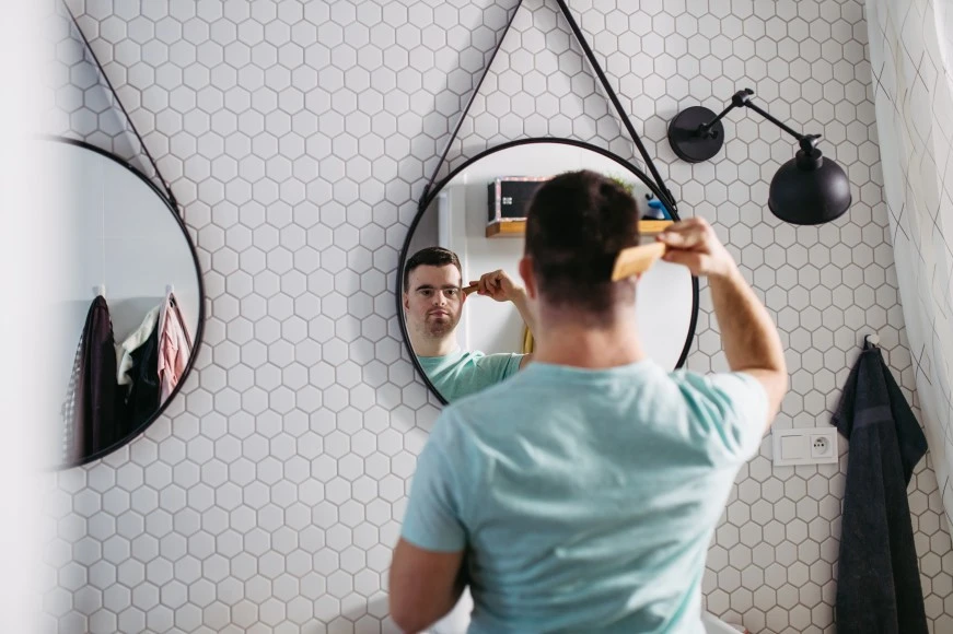 Disabled man with down syndrome brushing hair in mirror in bathroom at home