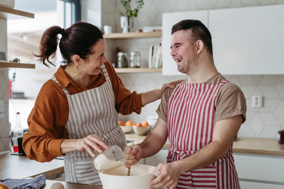 Disabled man with down syndrome in kitchen with support worker learning to cook